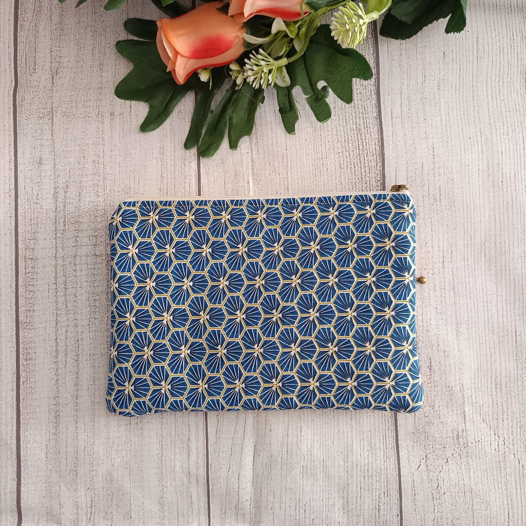 Organizador de bolso plano con estampado geométrico azul y blanco y tiradores de cremallera metálicos sobre fondo rústico"