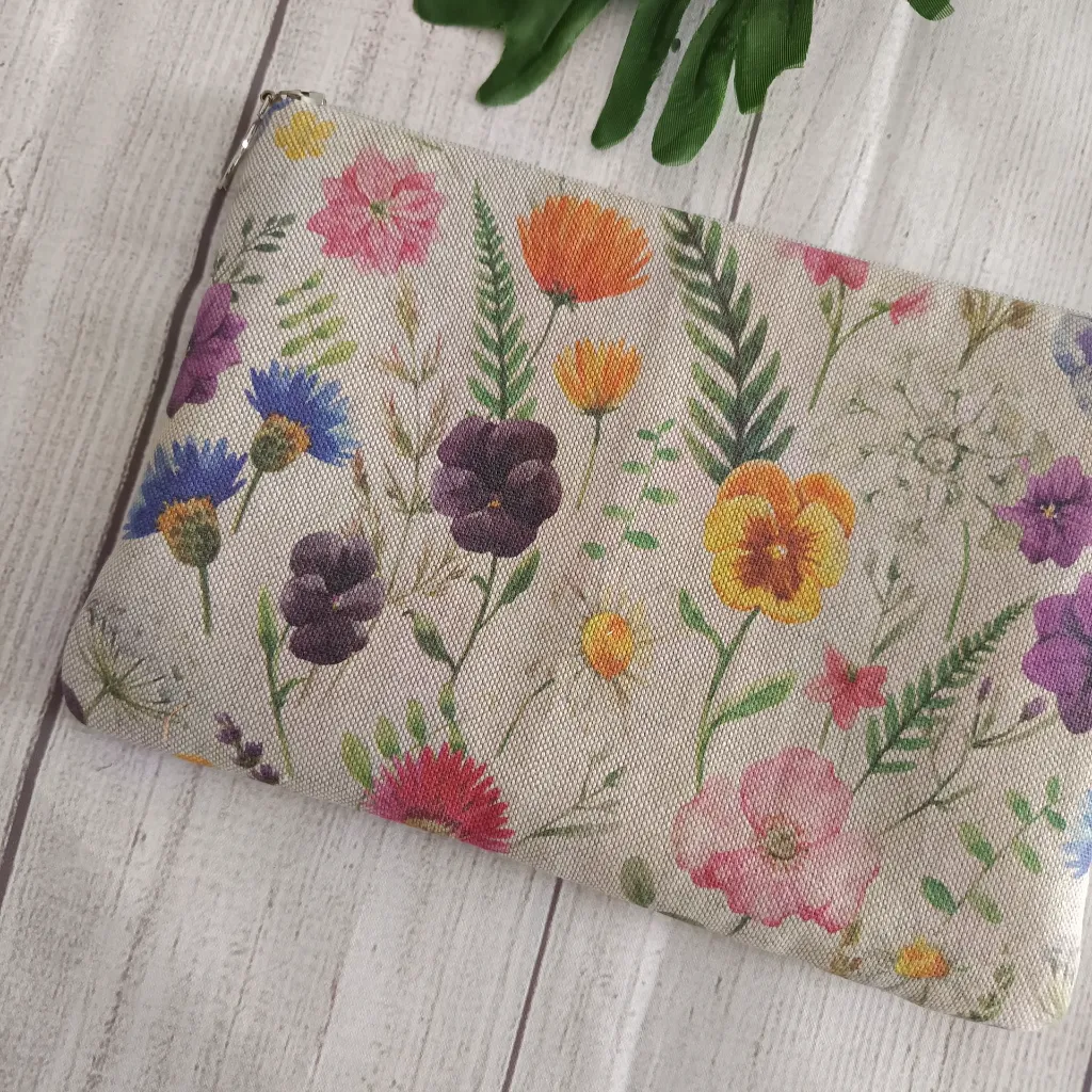 Neceser plano de tela floral con cremallera sobre fondo claro