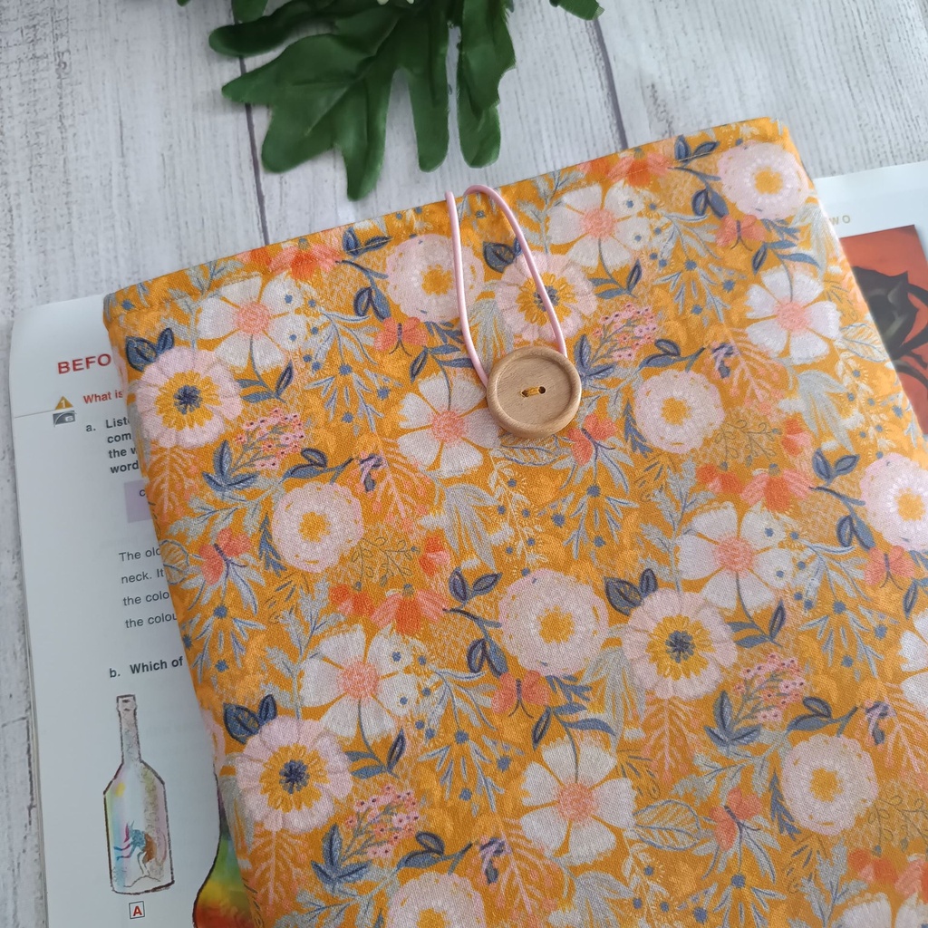 Funda para libro hecha a mano con tela floral en tonos mostaza, interior rosa y cierre con botón