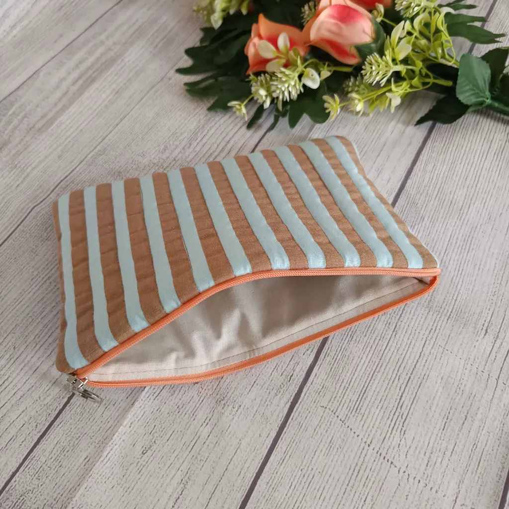 Detalle de neceser plano de tela con estampado de rayas turquesa y marrón hecho a mano.
