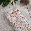 Funda de gafas artesanal hecha a mano en tela de algodón con estampado floral multicolor en rosa, naranja, lila y verde sobre fondo blanco, con cierre a presión rojo, fotografiada sobre madera clara junto a unas gafas de sol doradas