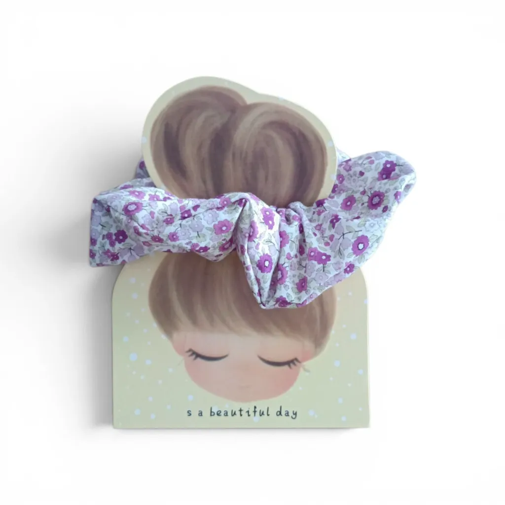 Coletero artesanal hecho a mano con tela floral en tonos  lilas sobre fondo blanco